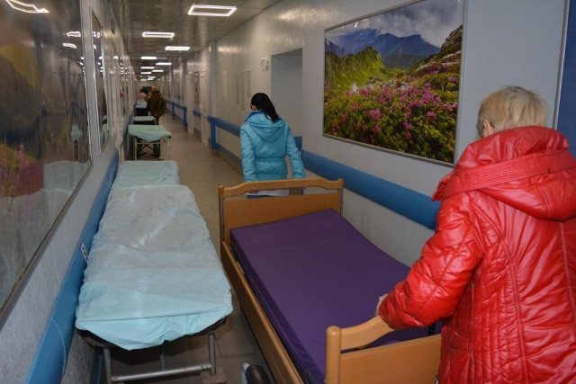 Zwei ukrainische Krankenhausmitarbeiterinnen schieben ein Bett auf dem Flur der Krankenstation zu dem Zimmer, wo es gebraucht wird.